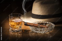 a glass of whiskey and a hat on a wooden table