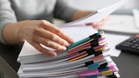 a person is holding a stack of papers on a desk