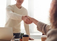 a man and woman shaking hands in front of a laptop